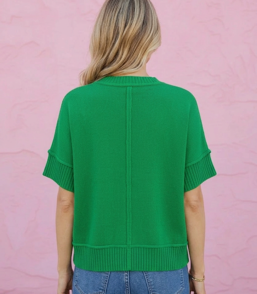Person wearing a green sweater and blue jeans against a pink wall