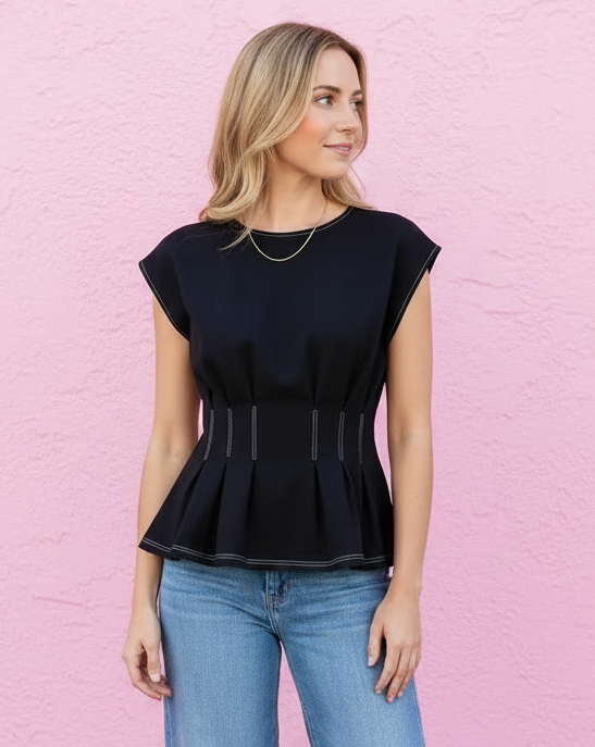 Woman wearing a black peplum top and blue jeans against a pink wall