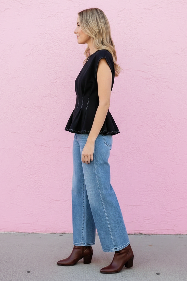 Woman wearing a black sleeveless top and blue jeans against a pink wall.