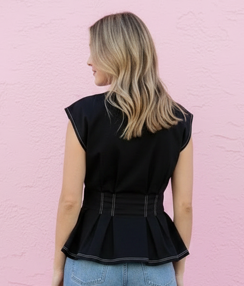 Person wearing a black sleeveless top and blue jeans against a pink wall