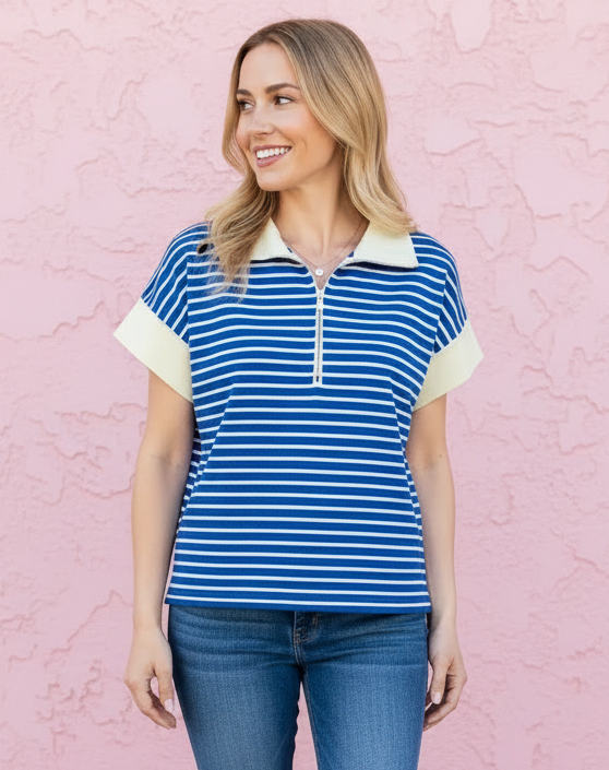 Woman wearing a blue and white striped shirt and jeans standing against a pink wall.
