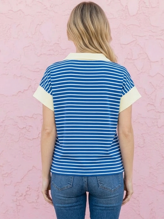 Person wearing a blue and white striped shirt and jeans standing against a pink wall.