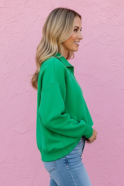 Woman wearing a green sweater and blue jeans against a pink wall