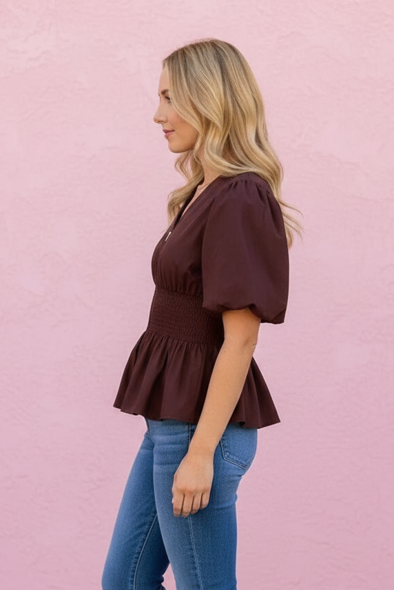Woman wearing a brown top and blue jeans against a pink wall