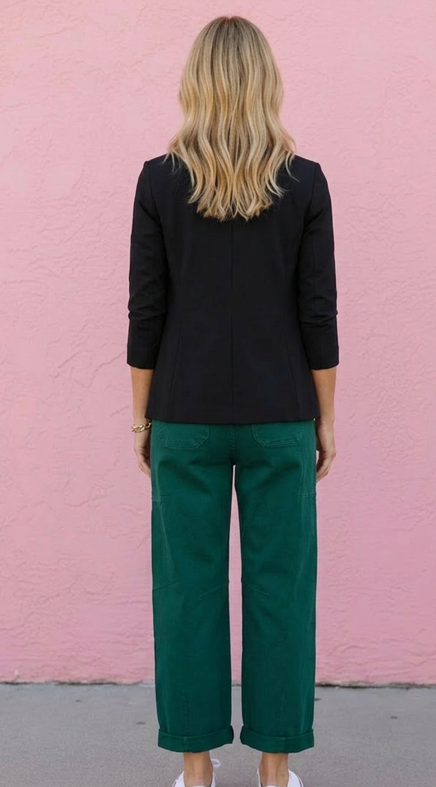 Person wearing a black top and green pants standing against a pink wall.