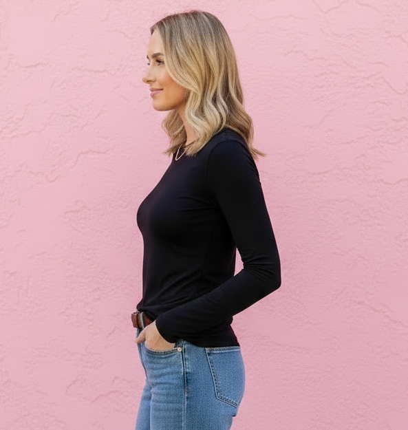 Woman wearing a black top and blue jeans against a pink wall