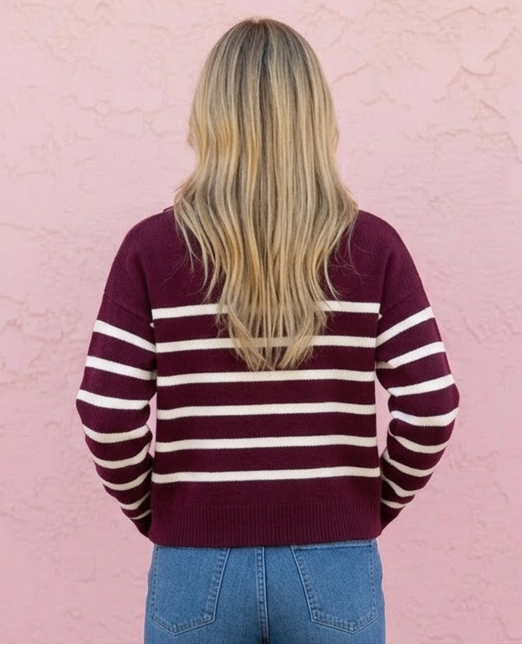 Person wearing a striped sweater and blue jeans against a pink wall