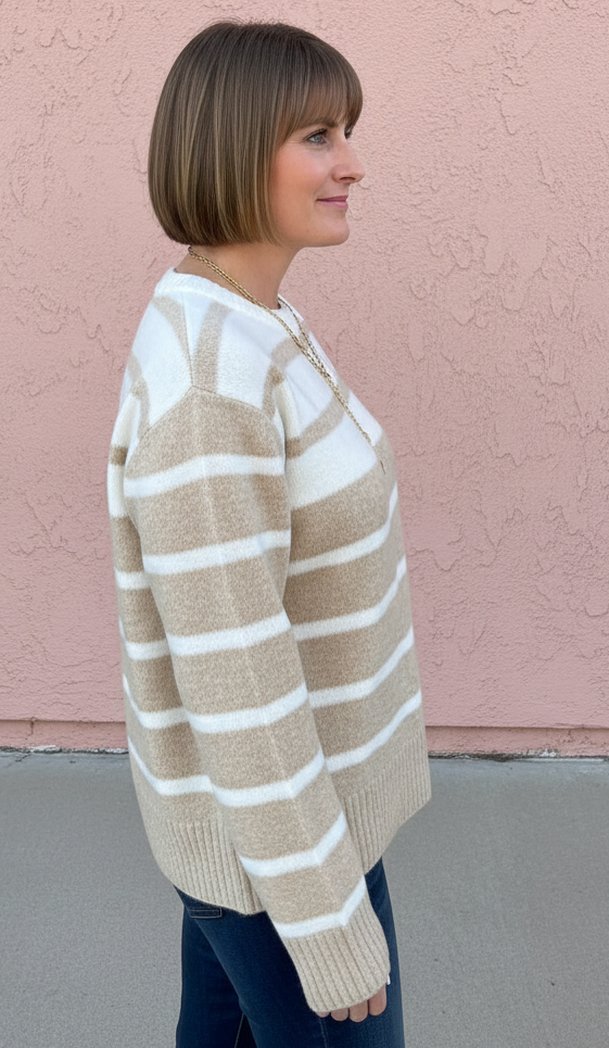 A woman with a short brown bob haircut is shown in profile, wearing a beige and white horizontally striped knit sweater and dark blue jeans, standing against a textured pink stucco wall.
