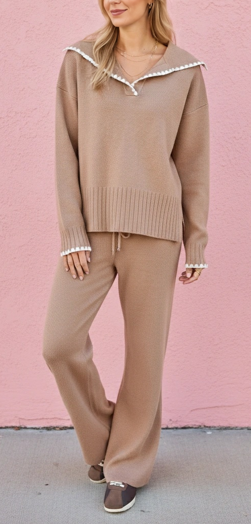 A woman modeling a matching beige knit lounge set consisting of a long-sleeve sweater with a decorative white ruffled collar and matching wide-leg pants, standing against a pink stucco wall.