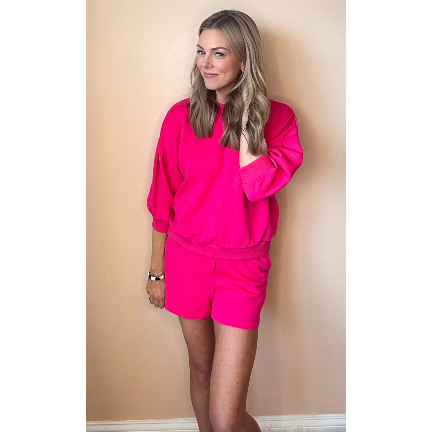 Woman wearing a bright pink outfit against a beige wall