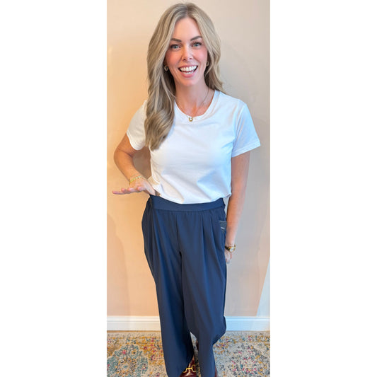 Woman wearing a white t-shirt and blue pants against a beige wall.